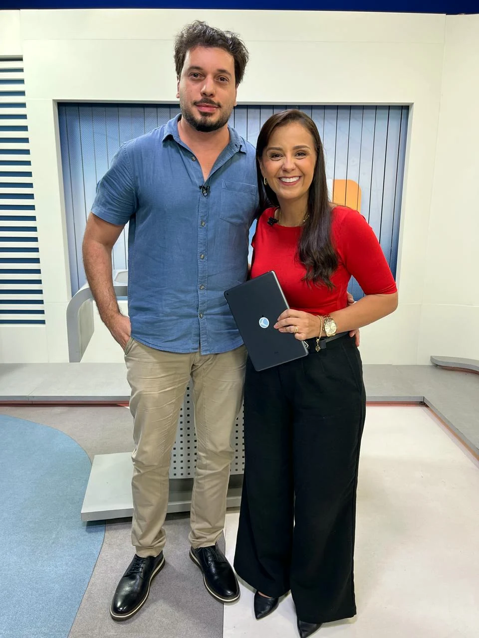 Dr. Rossini Monteiro de camisa azul-clara com a apresentadora de vermelho no estúdio do MGTV.